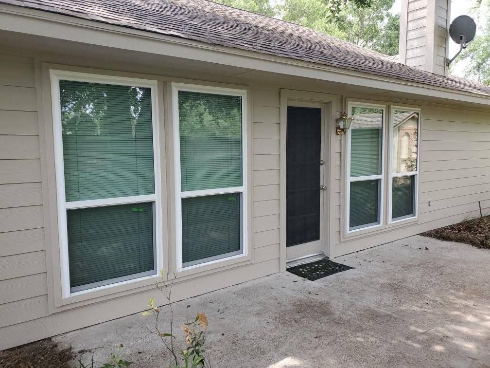 Exterior of a beige house with white-framed windows and a dark door on a concrete patio.