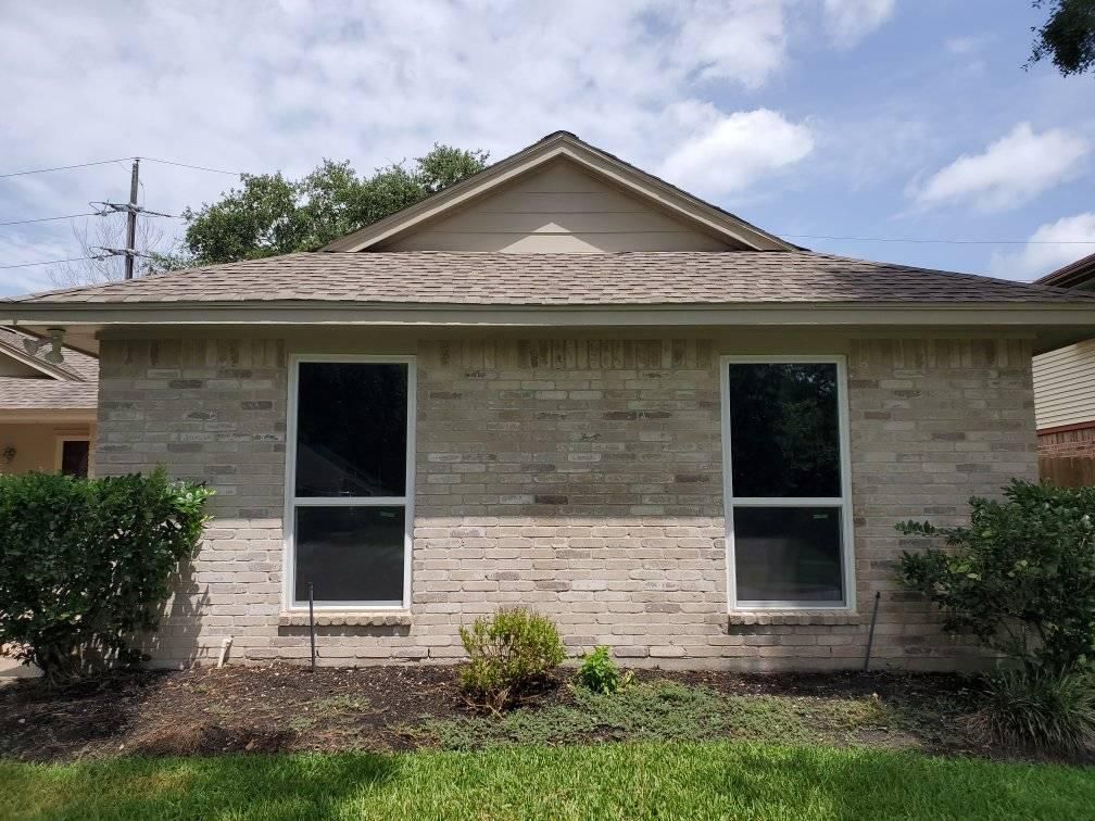 Exterior of a brick building with two windows under a roof, greenery in the foreground.