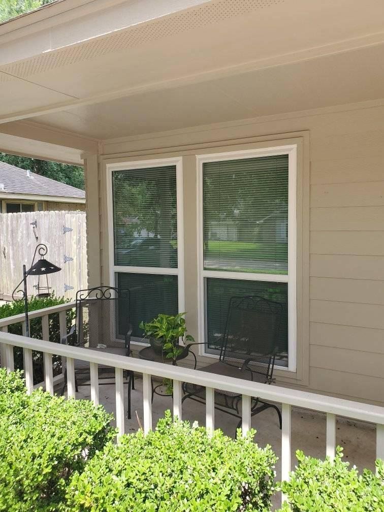 Front porch with two large windows, black wrought iron furniture, and green bushes.