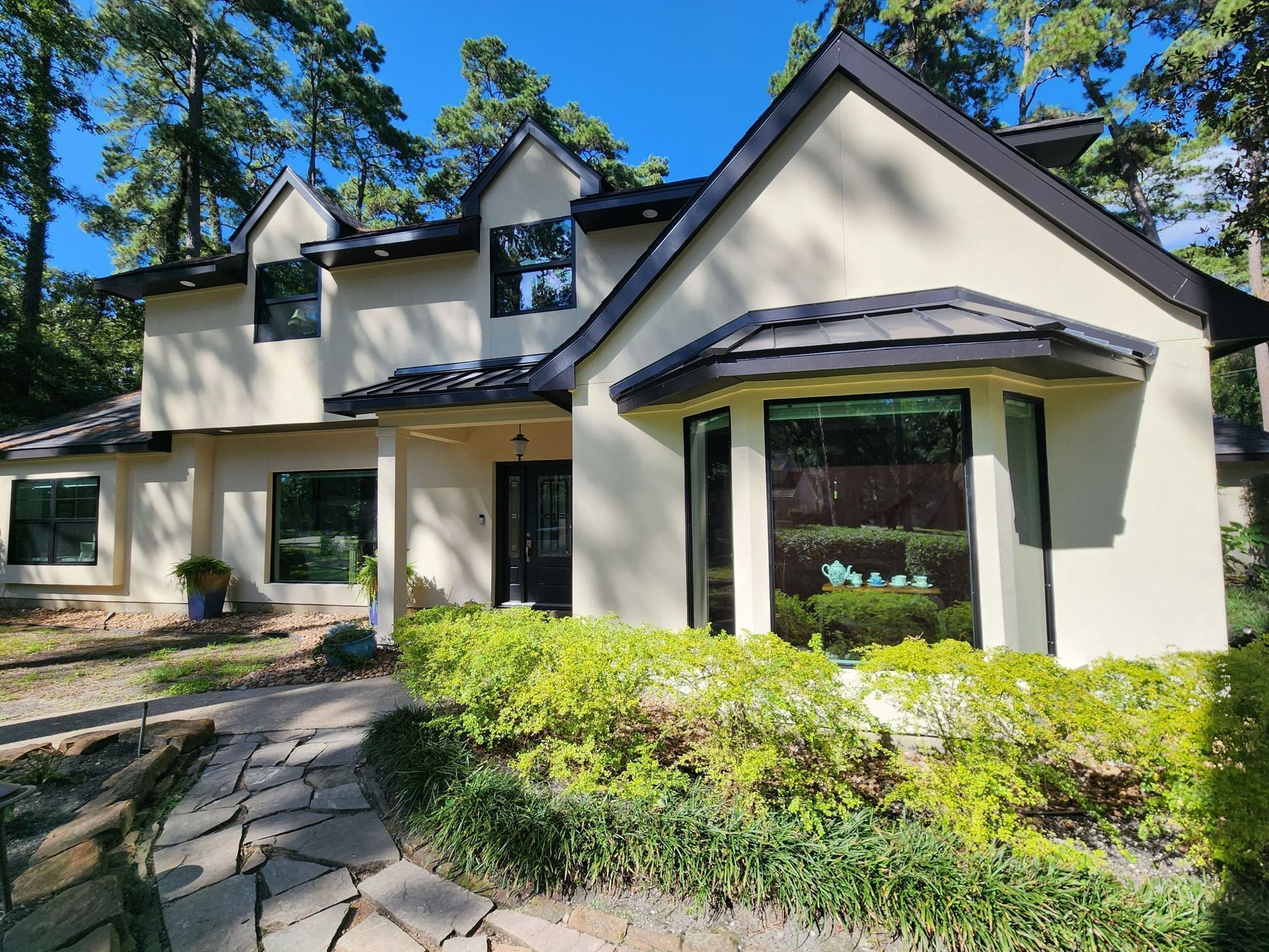 Beige house with dark roof, surrounded by trees and a stone walkway.