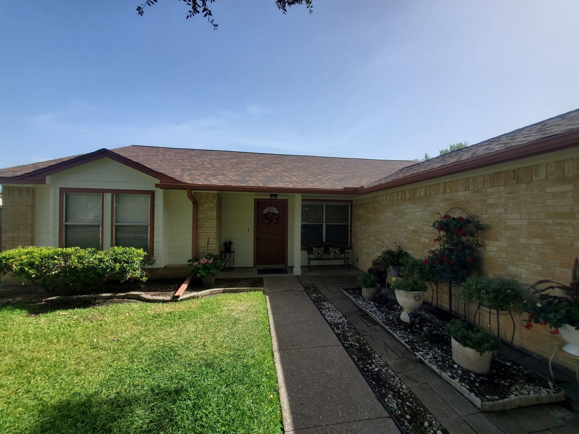 A one-story beige house with a brown roof and a walkway leading to a brown door.