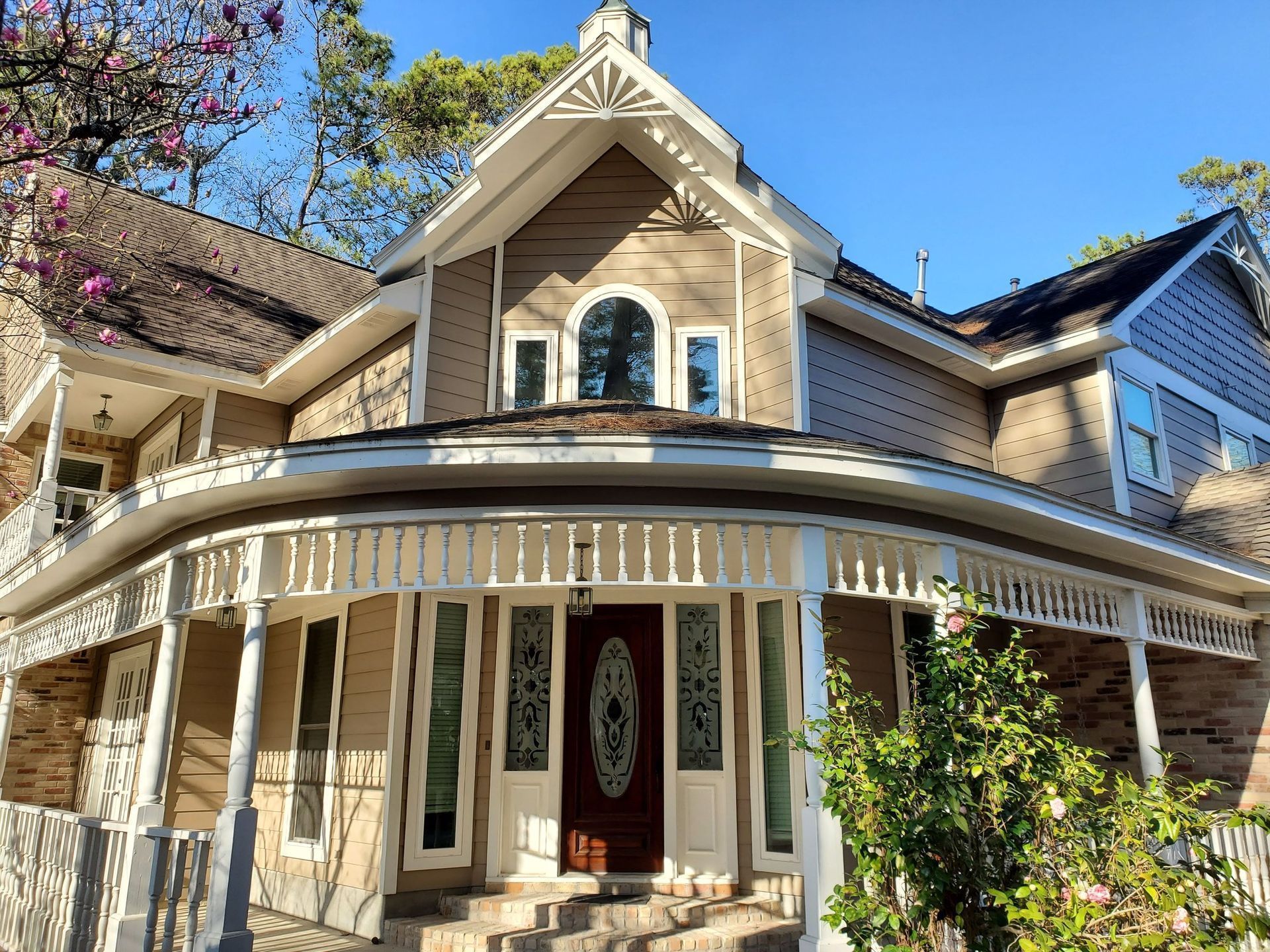 Two-story house with a wraparound porch, brown siding, and arched window.
