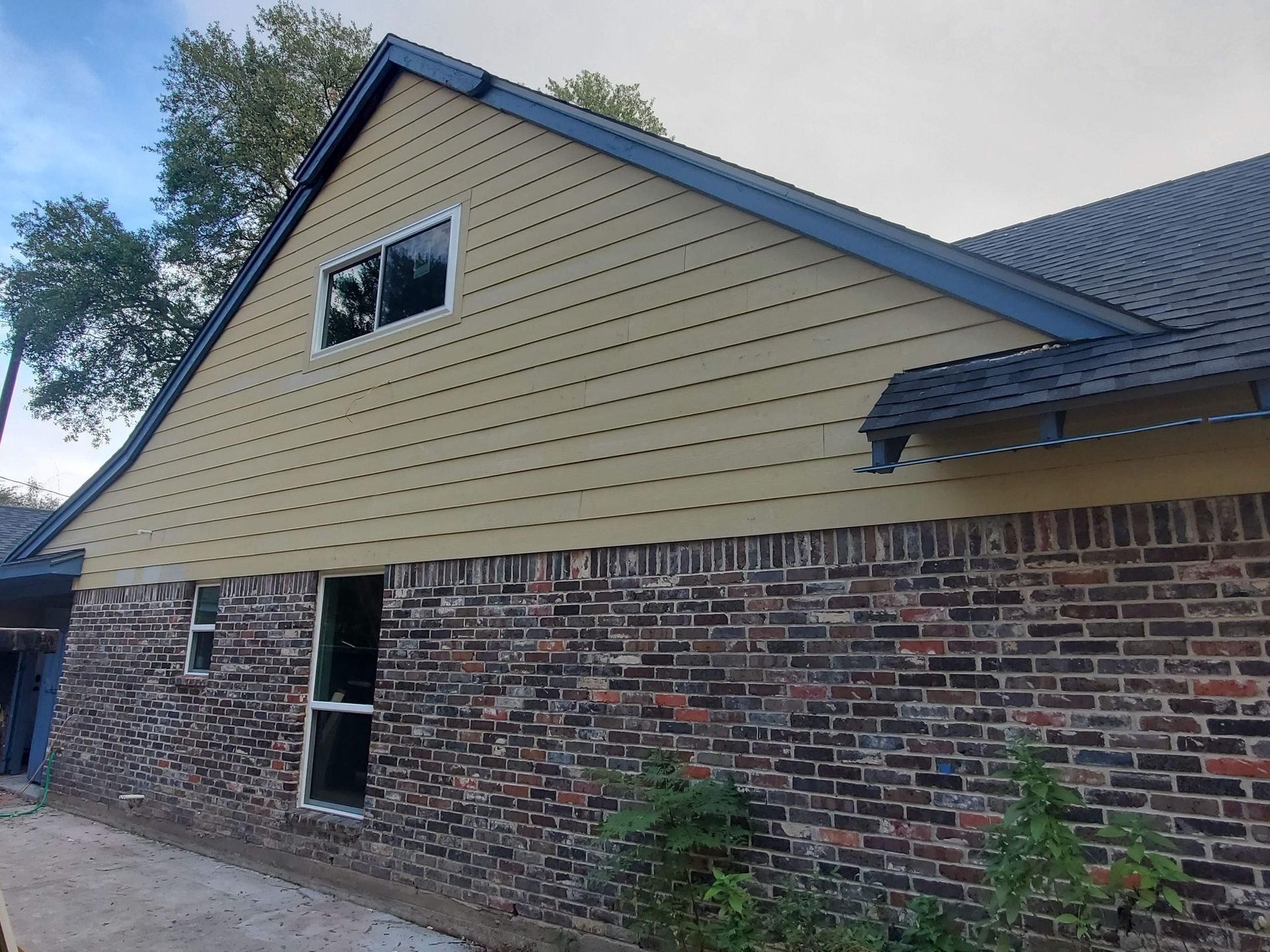 Brick and tan sided house with dark blue roof and trim; two windows.