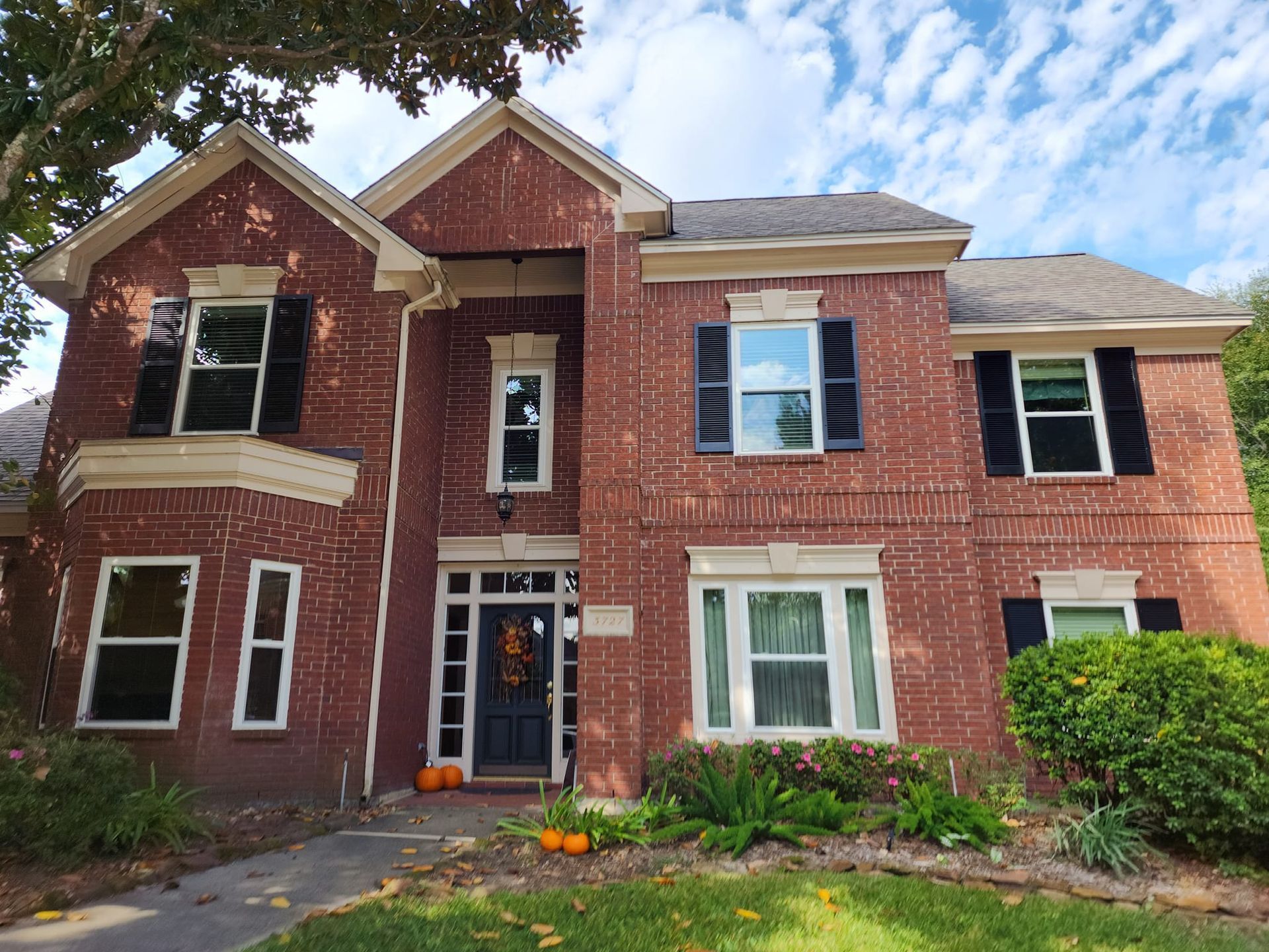 Brick house with black shutters, blue door, pumpkins on porch, cloudy sky.