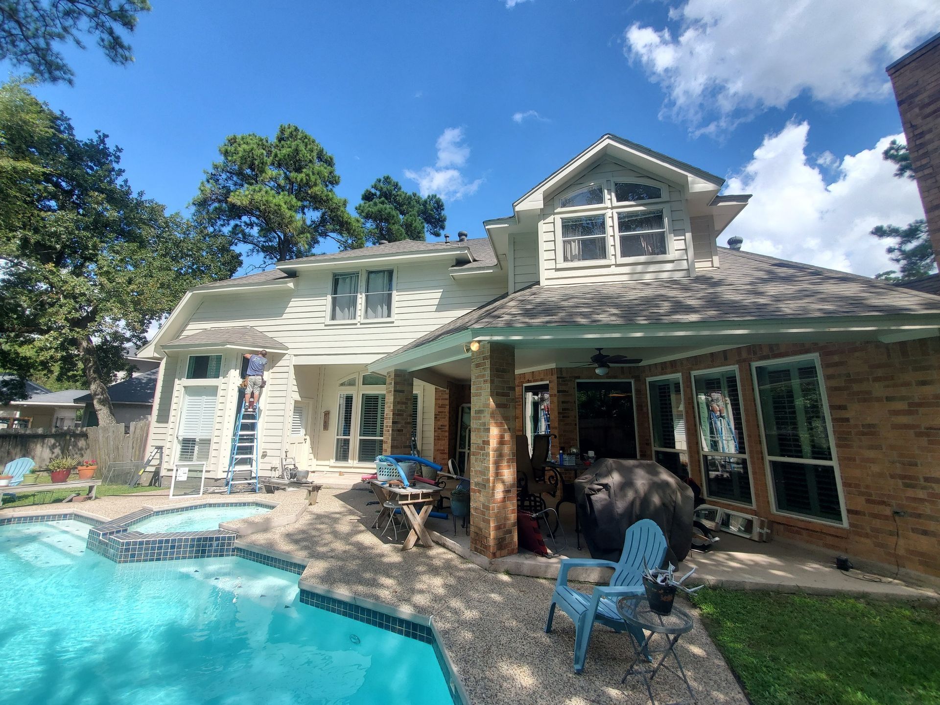 House exterior with pool. Light-colored siding, brick accents, and a covered patio area. Blue sky with clouds.