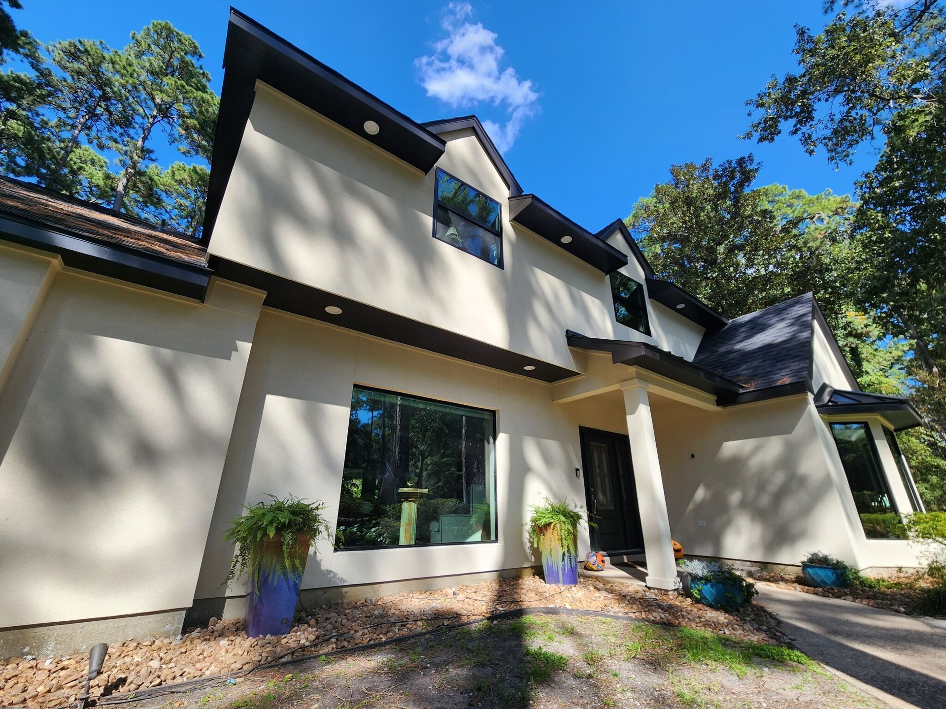 Two-story house with light stucco walls, dark trim, and blue planters in front. Sunny day.