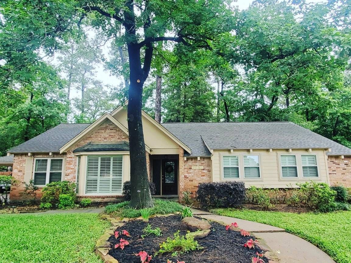 A brick and tan single-story home with a dark gray roof, lush green yard, and a curved walkway.