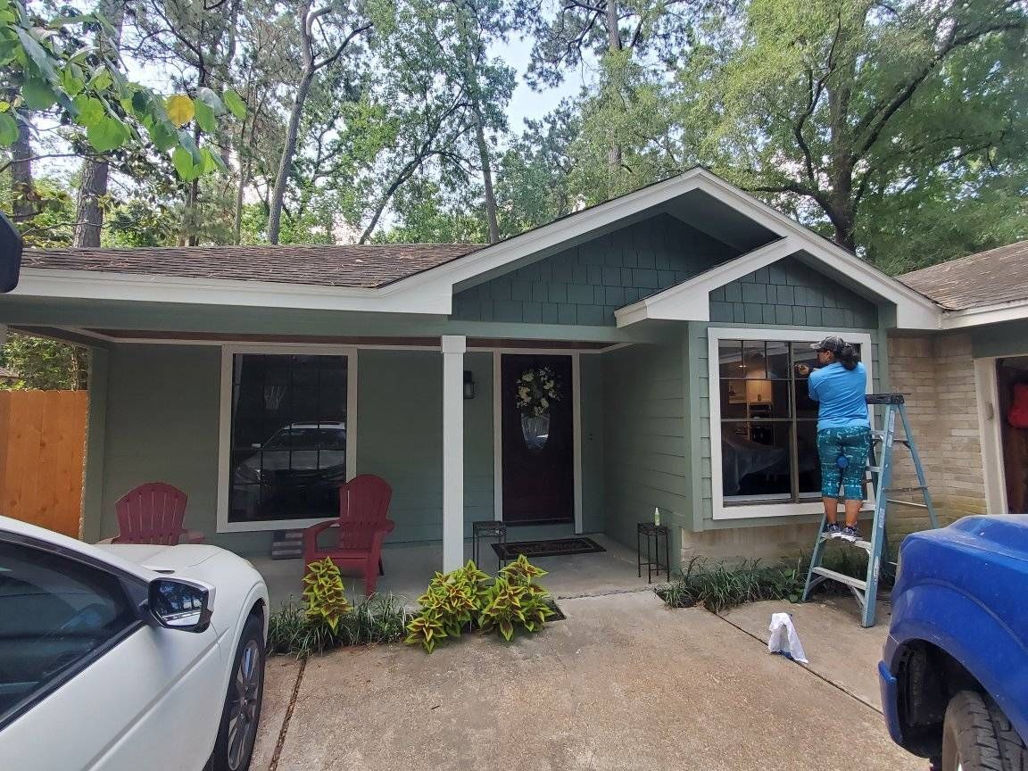 Person cleaning window on a green house. A white car and blue truck are parked in front.