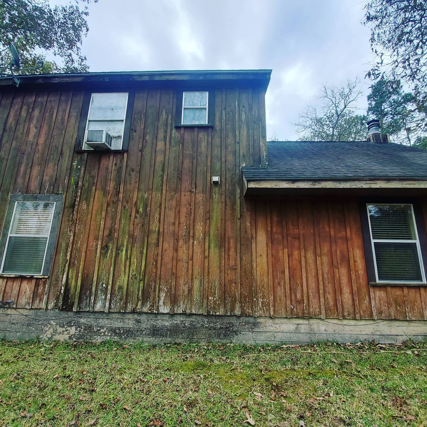 Wooden house with weathered siding, windows, and an air conditioner, set against a cloudy sky.