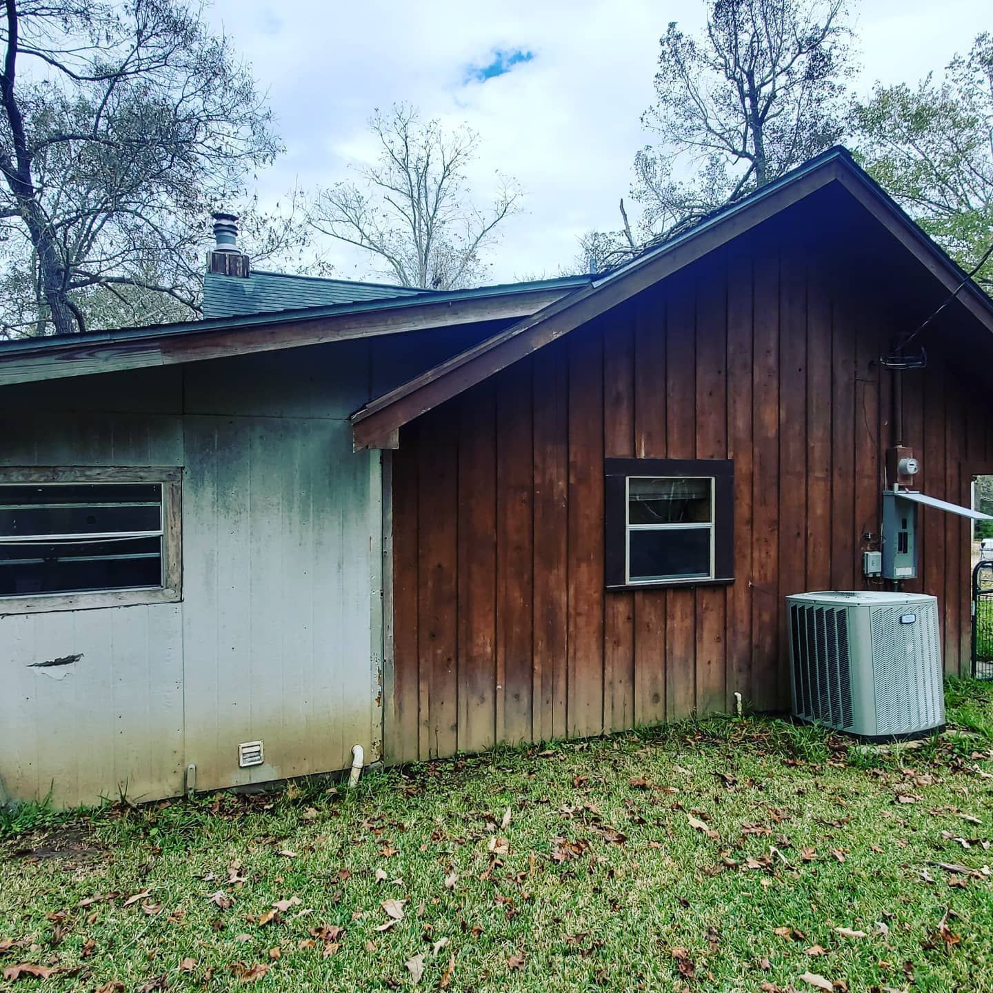 Side view of a weathered wooden house with a small window, an air conditioning unit, and a metal roof.