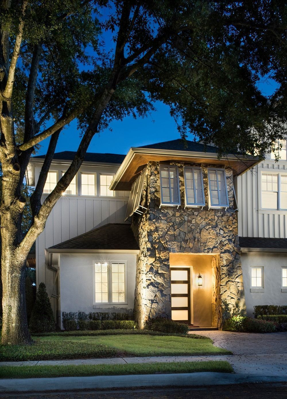Lit stone house with modern door under tree at night.
