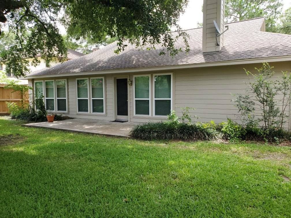 Beige house exterior with windows, door, and patio area, surrounded by green grass and landscaping.
