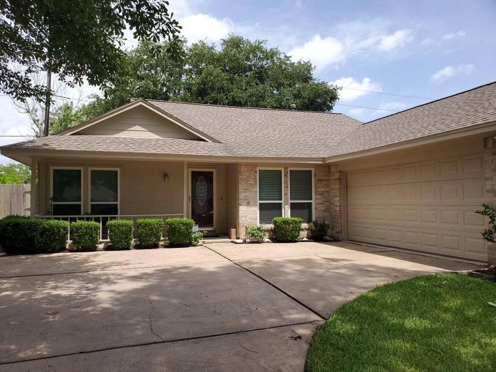 Beige ranch-style house with a brown roof and a concrete driveway on a sunny day.