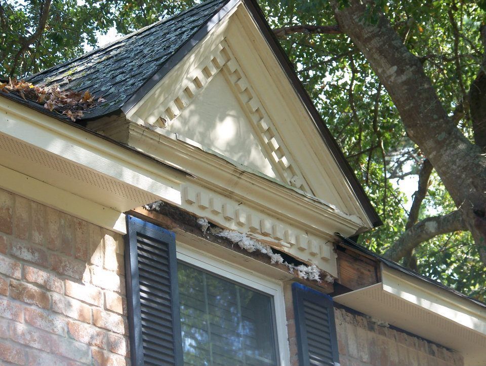 Close-up of a house's roofline with a triangular gable, decorative trim, and visible damage.