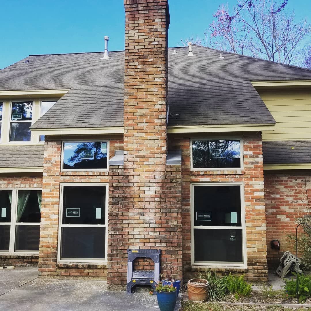 Back of a house with a brick chimney, gray roof, and new windows.