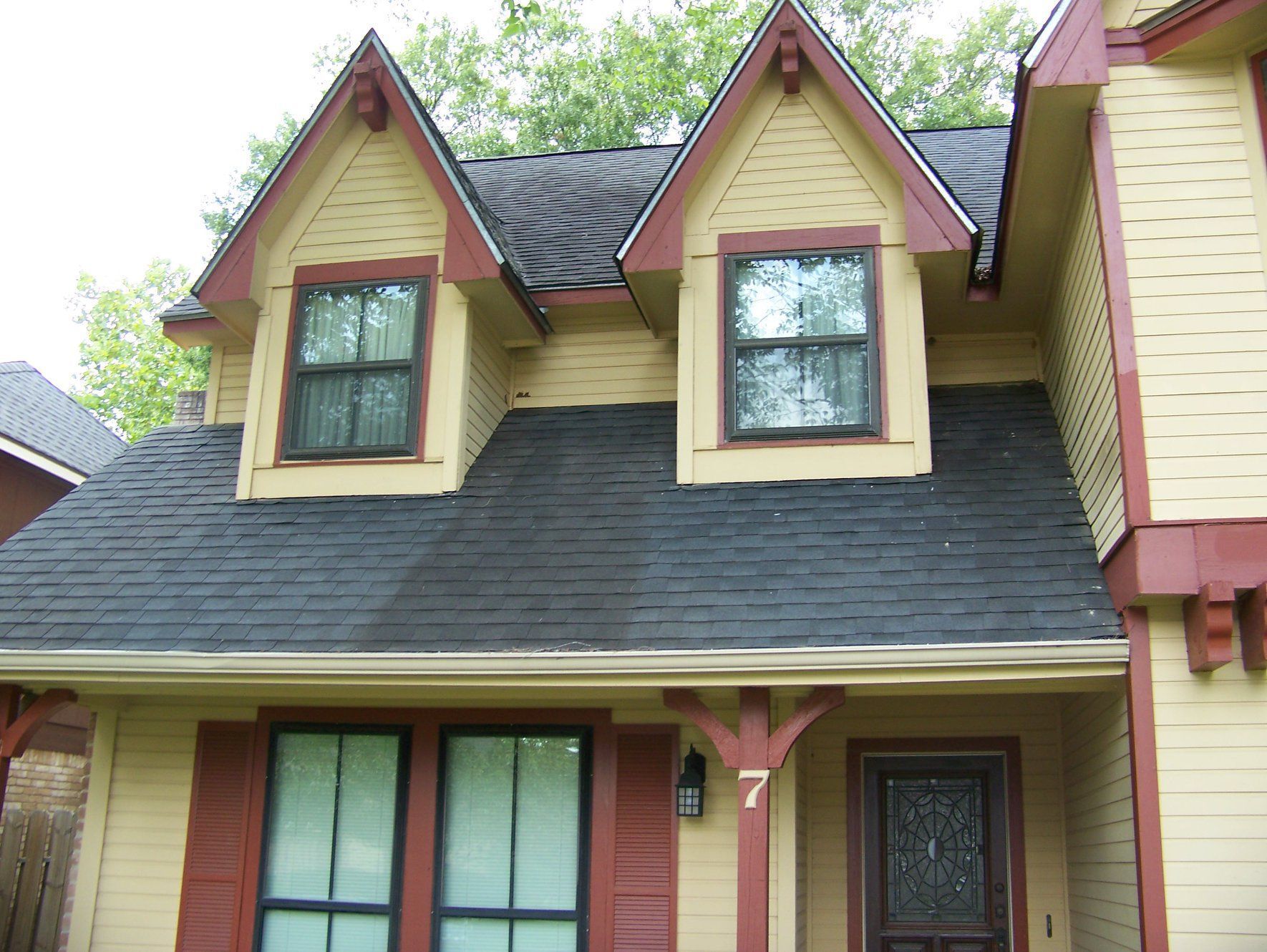 Yellow house with red trim, black roof, and two dormer windows.