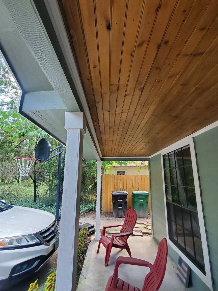 Porch with stained wooden ceiling, white pillars, red chairs, and a car.