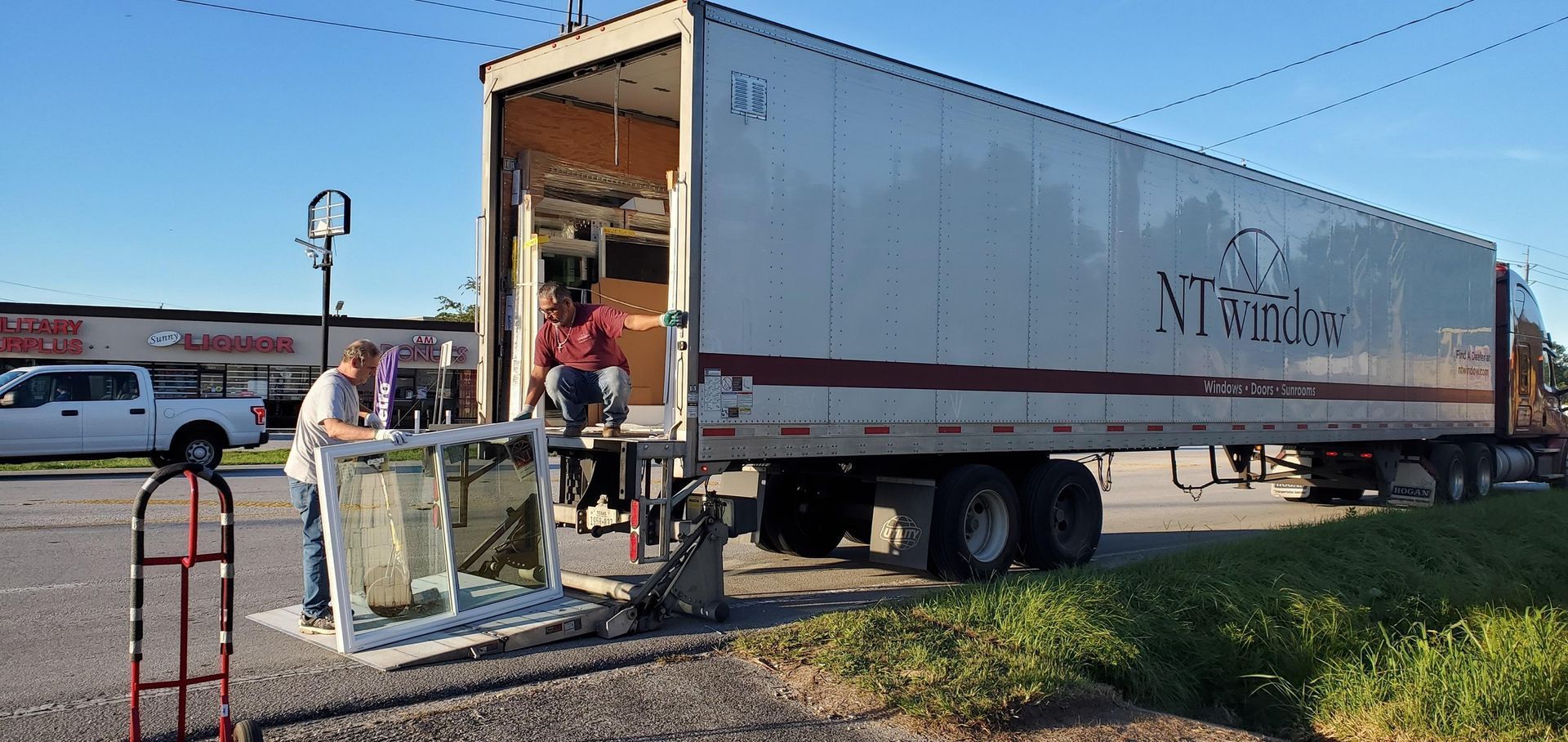 Two people unloading a large window from a semi-truck with 