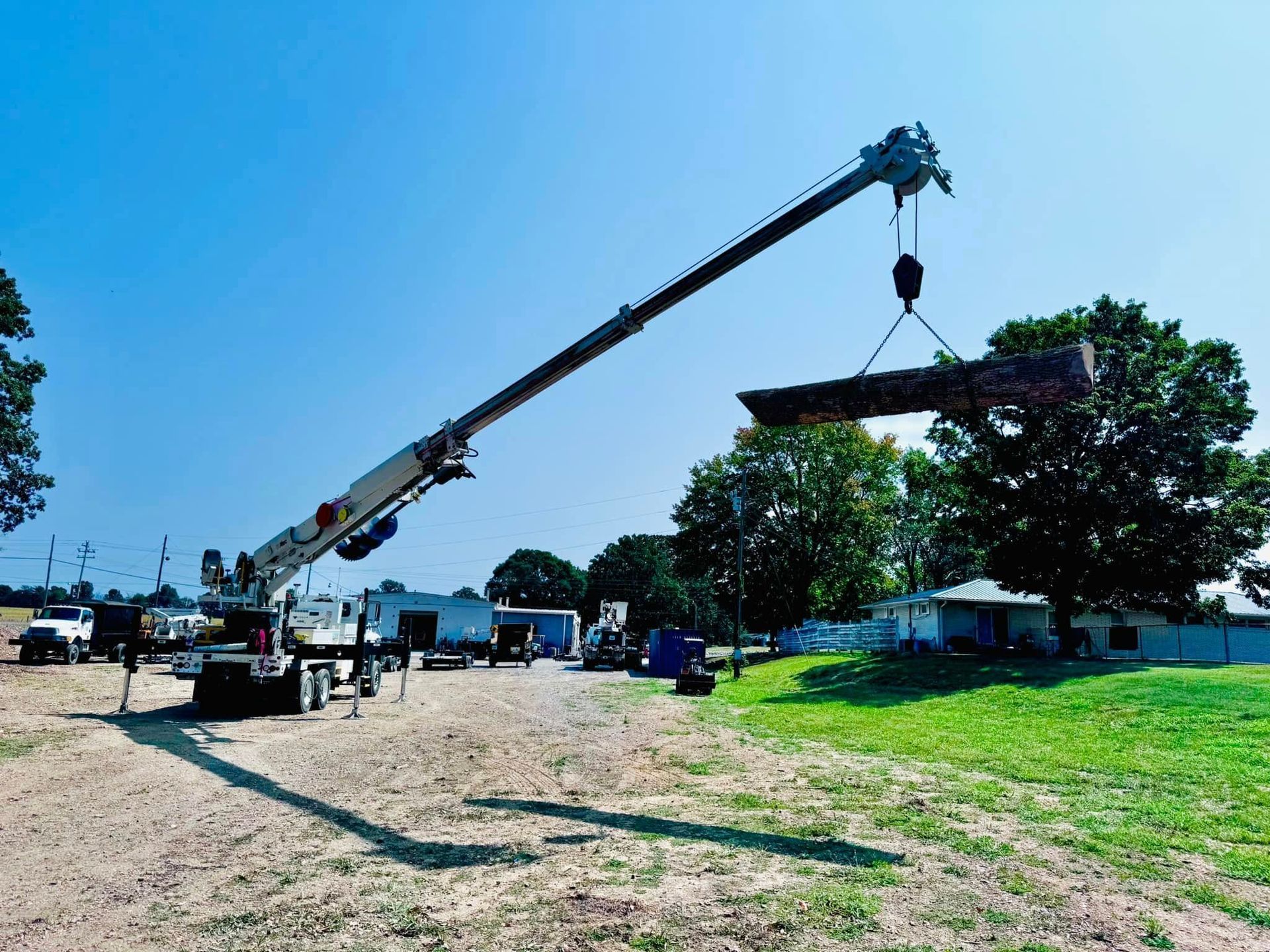 A crane is lifting a large piece of wood in a field.
