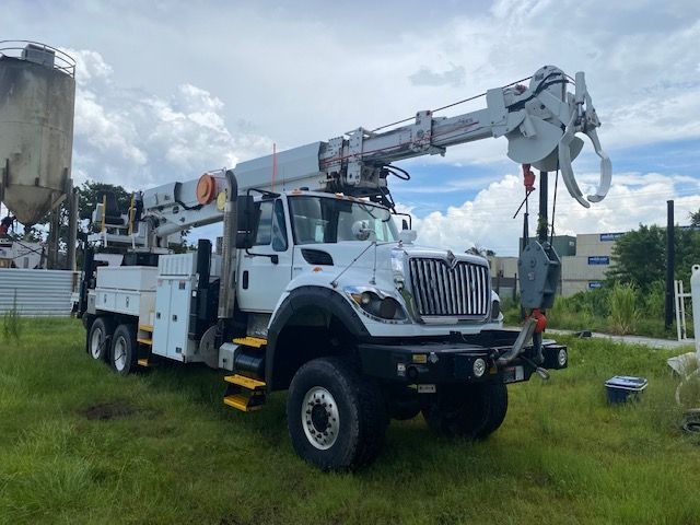 A white truck with a crane attached to it is parked in a grassy field.