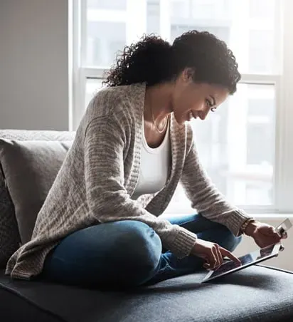 A woman is sitting on a couch using a tablet computer.
