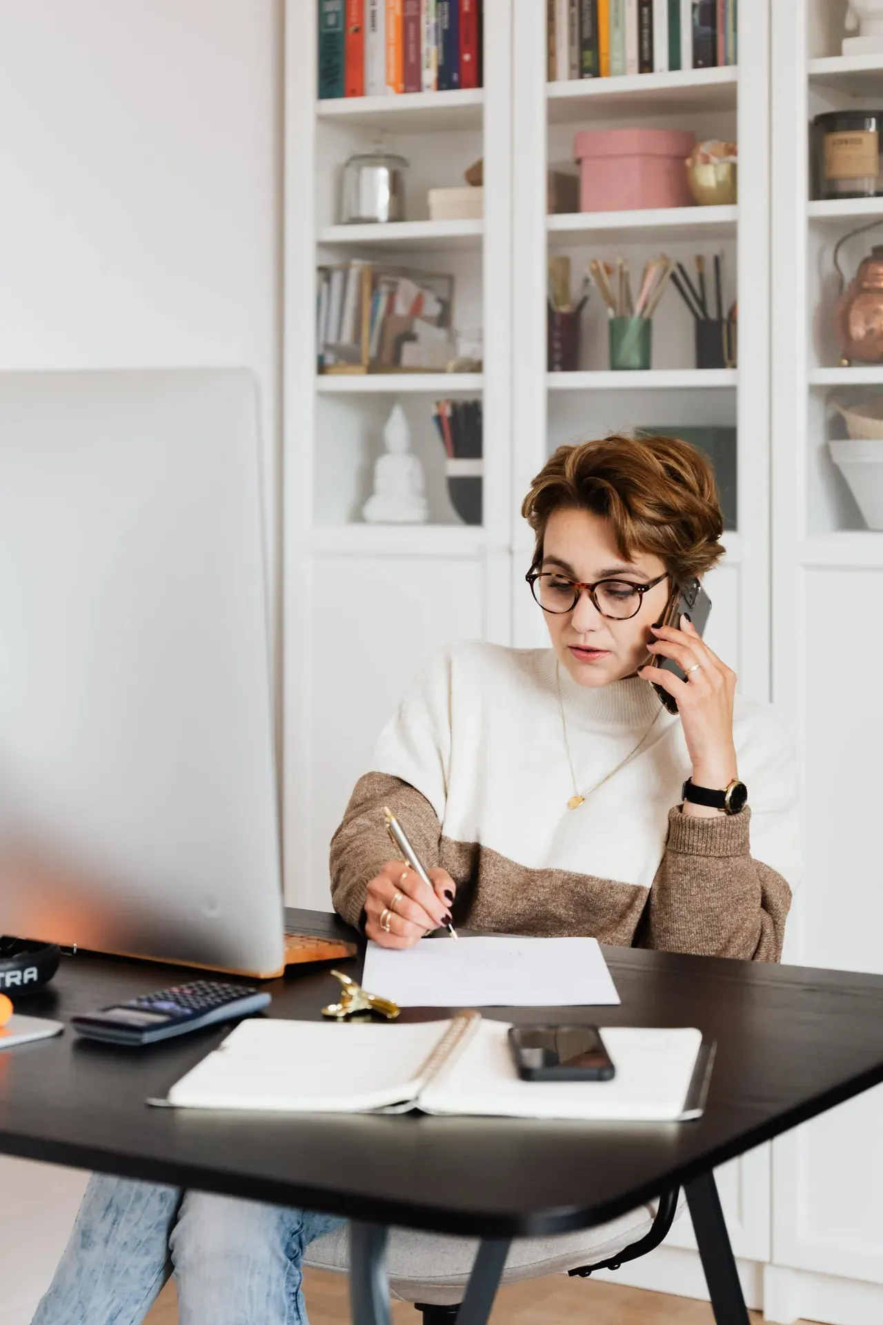 A woman is sitting at a desk talking on a cell phone.