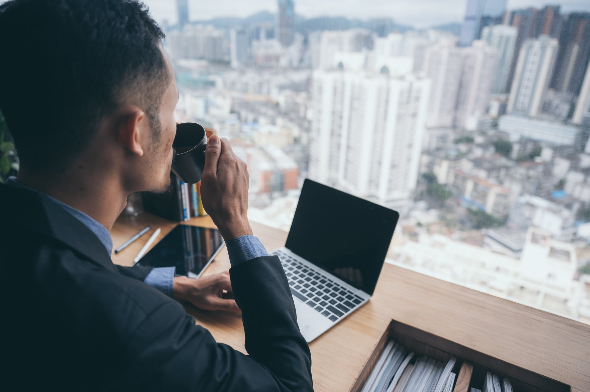 A man is sitting at a desk with a laptop and drinking coffee.