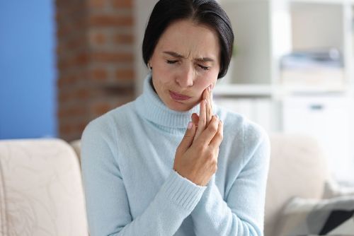 A woman is sitting on a couch with a toothache.