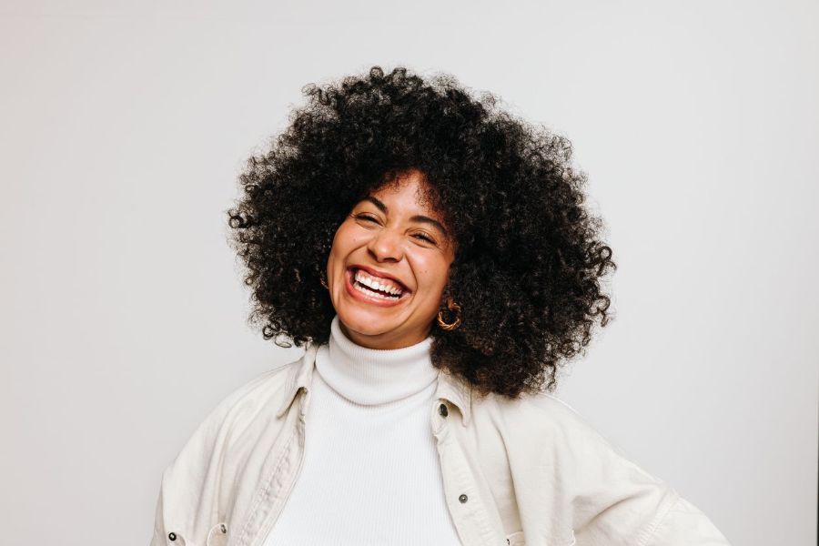 A woman with curly hair is smiling and laughing.