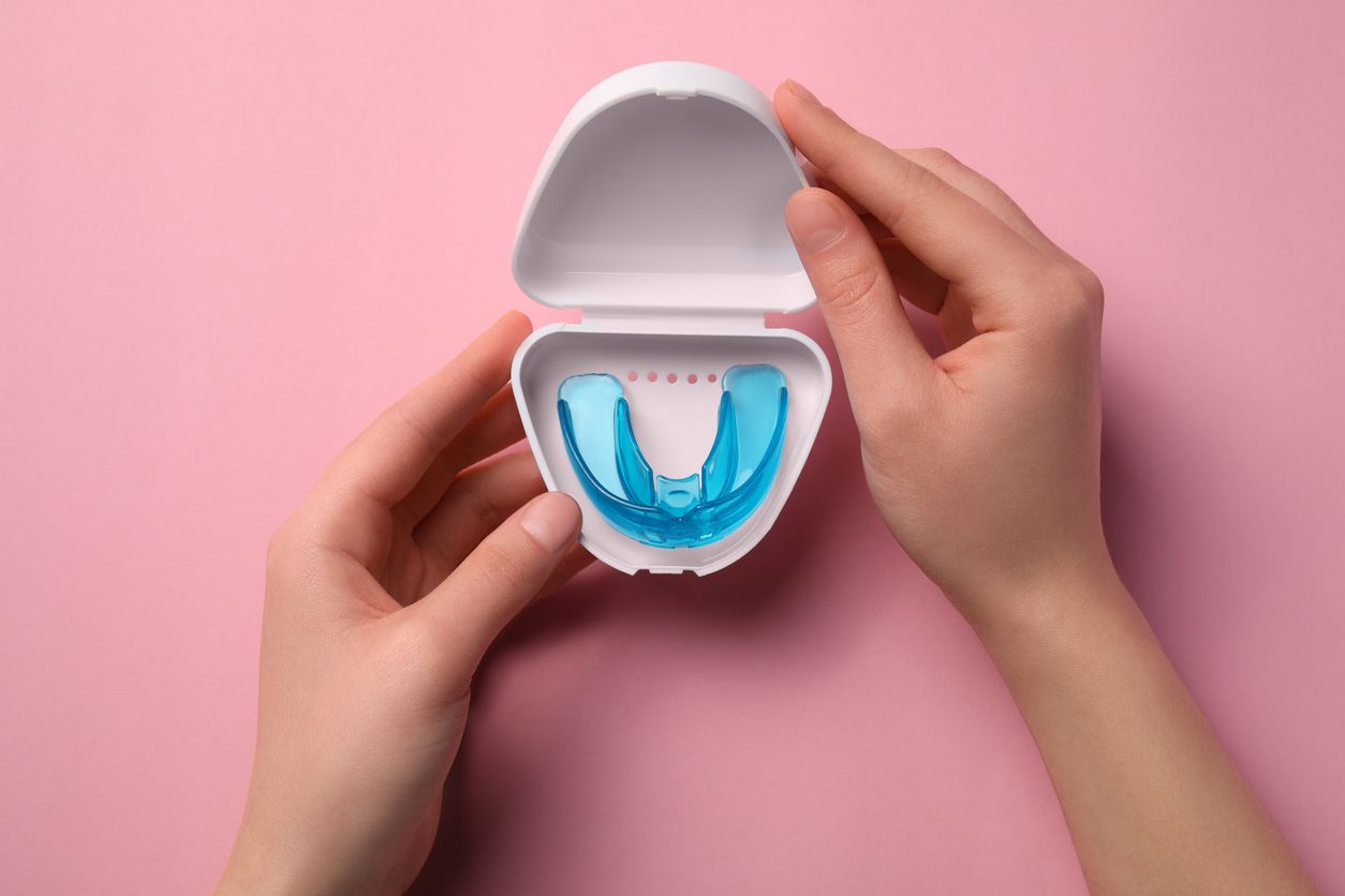 Hands opening a white case with a blue mouth guard on a pink background.