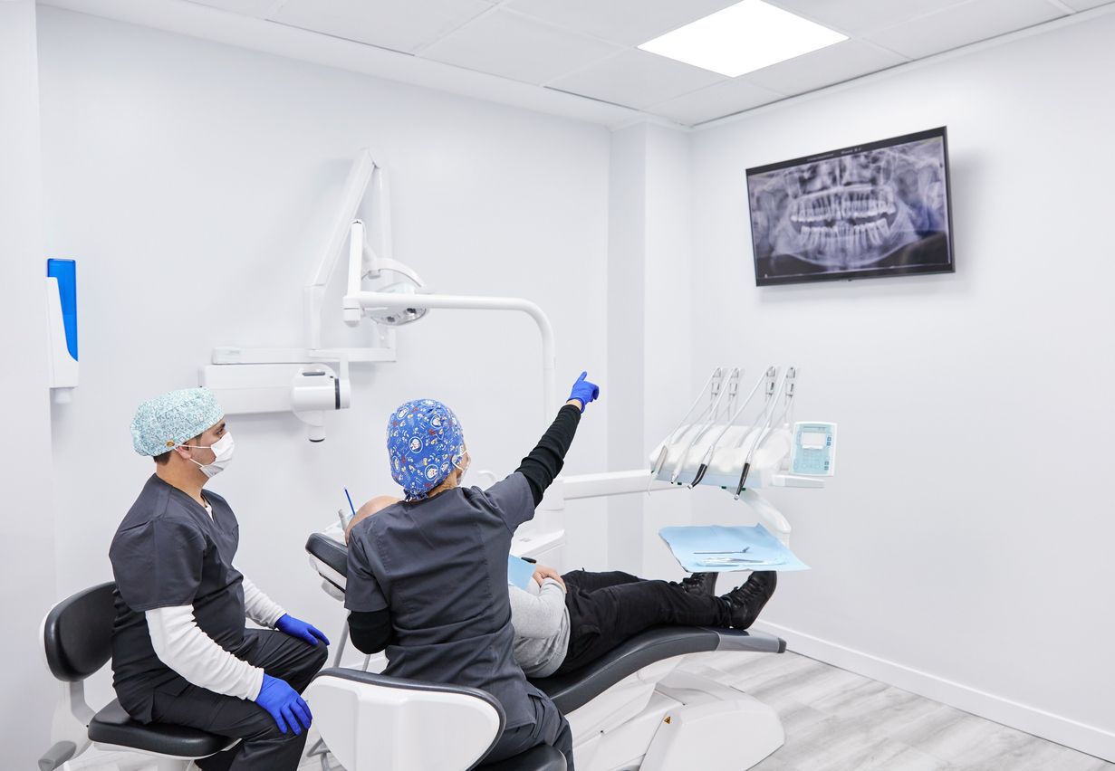 Dentist and assistant examining X-ray on a monitor in a bright white dental office.