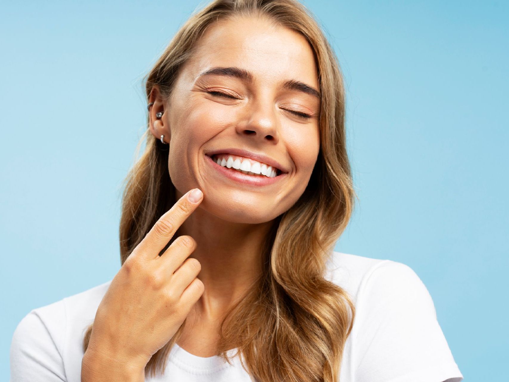 A woman is smiling and touching her face with her finger.