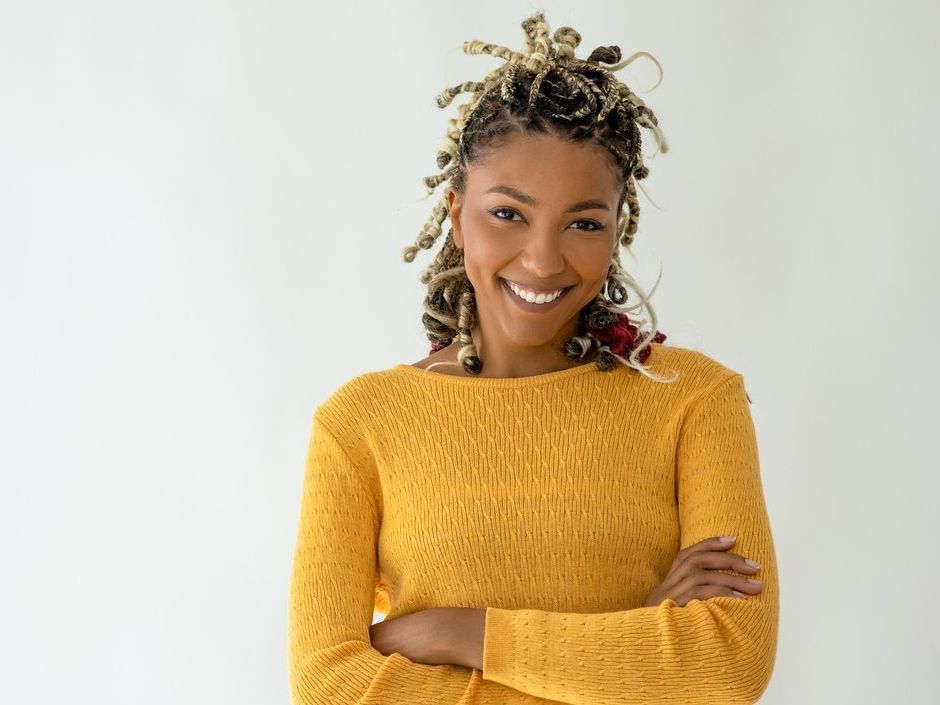 A woman in a yellow sweater is smiling with her arms crossed.