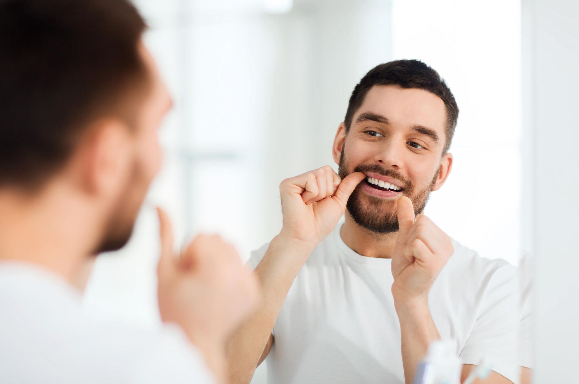 A man is flossing his teeth in front of a mirror.