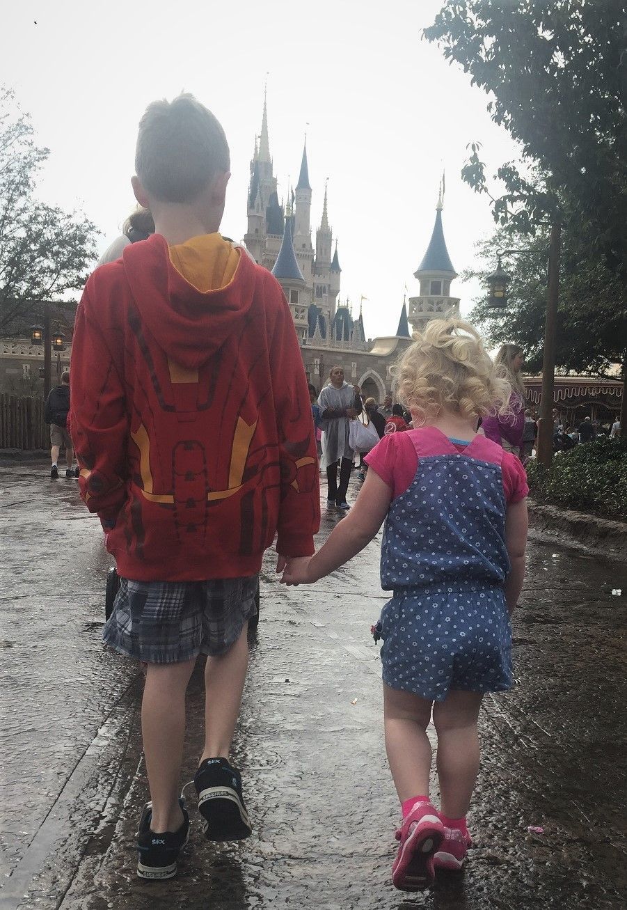 Two children holding hands while walking toward Cinderella Castle at Disney World.