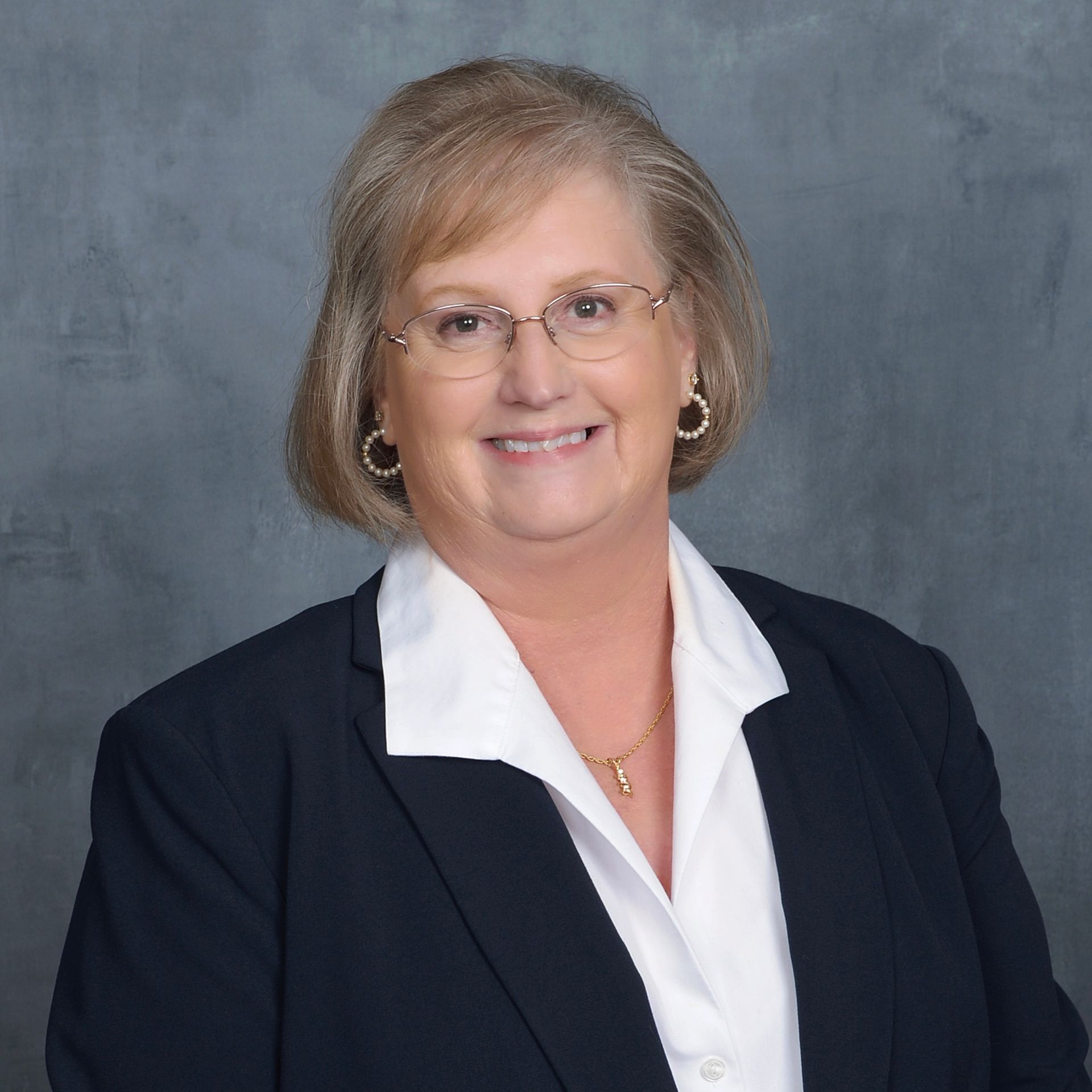 A woman wearing glasses and a black jacket is smiling for the camera.