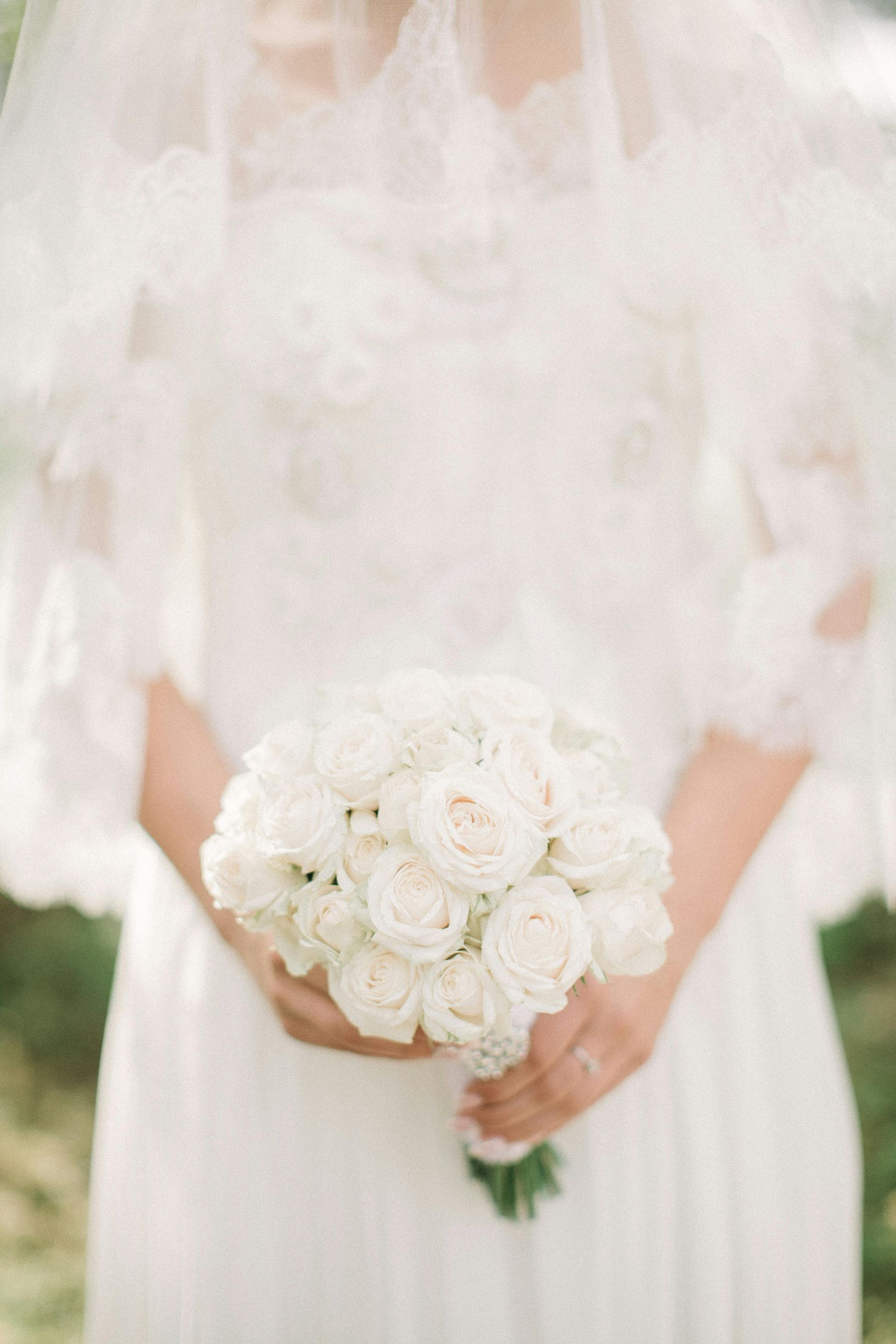 A bride in a white dress is holding a bouquet of white roses.