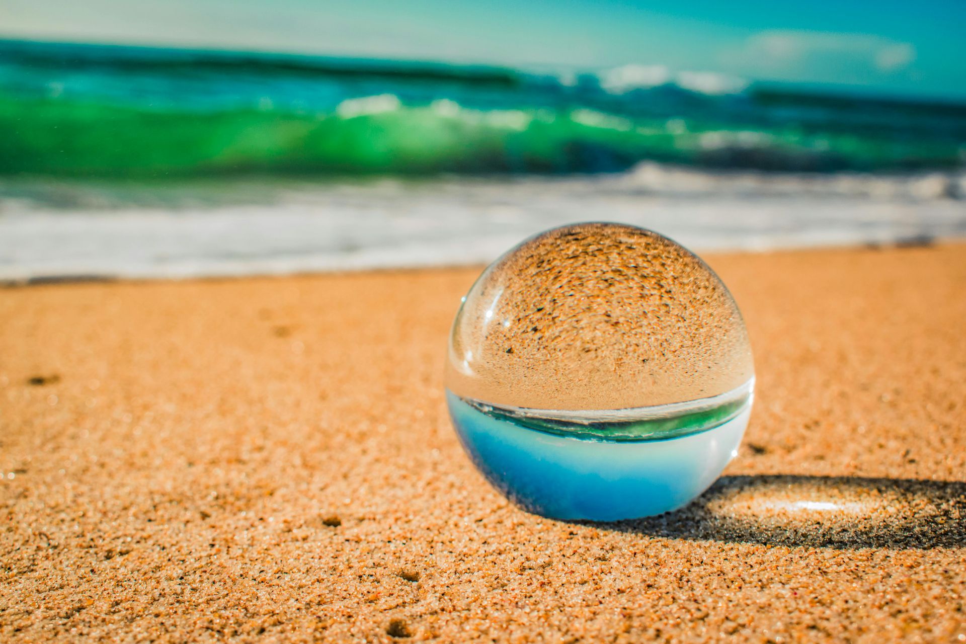 A glass ball is sitting on top of a sandy beach.