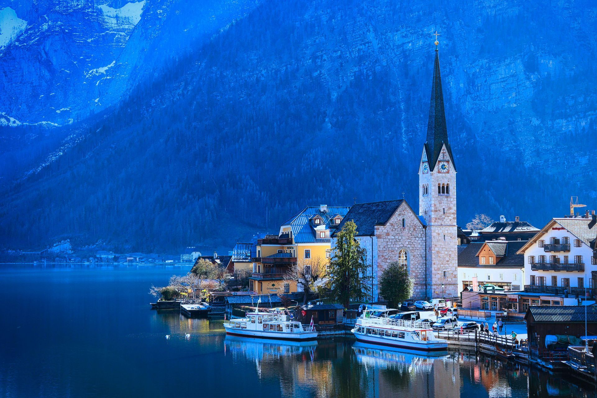 A dusk view of Hallstatt, Austria, featuring its iconic church spire and hillside buildings reflected in the calm lake.
