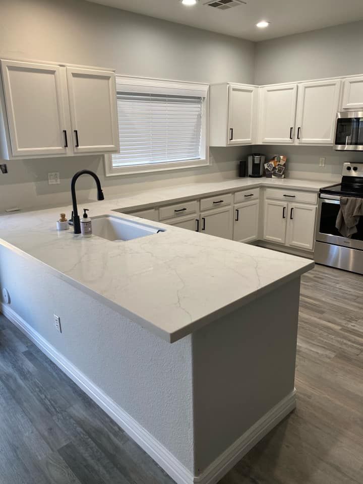 A kitchen with white cabinets , stainless steel appliances , a sink , and a large island.
