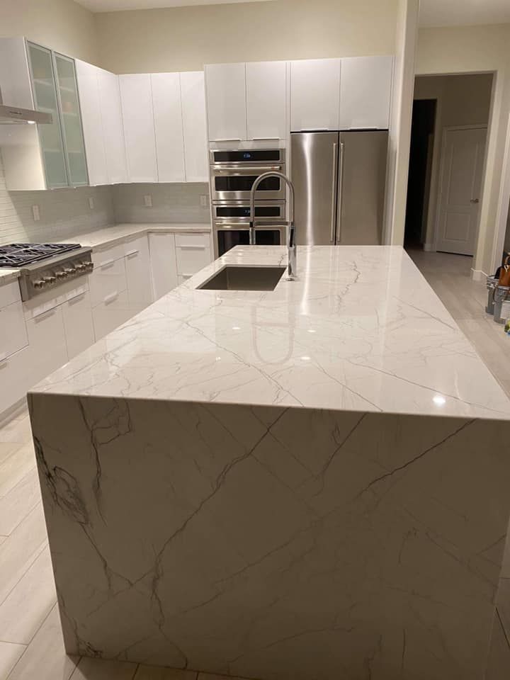 A kitchen with white cabinets , stainless steel appliances , a large island and a sink.