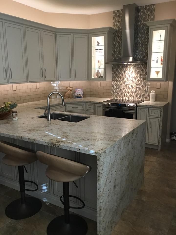 A kitchen with a large island , sink , stove and stools