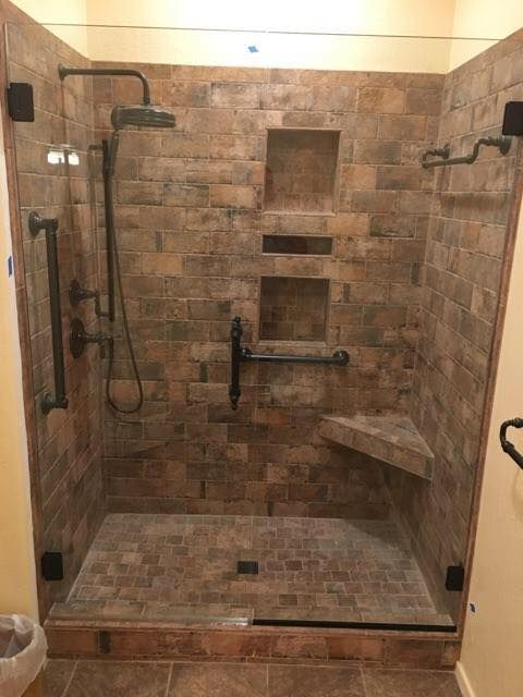 A walk in shower with a brick wall and a glass door.