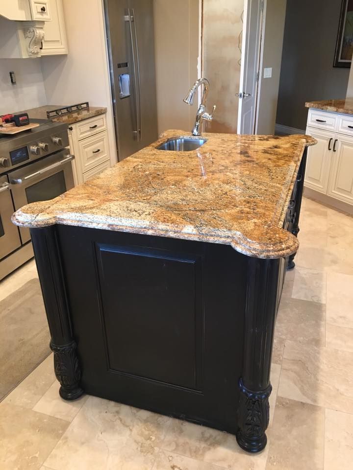A kitchen with a large island with a granite counter top and a sink.