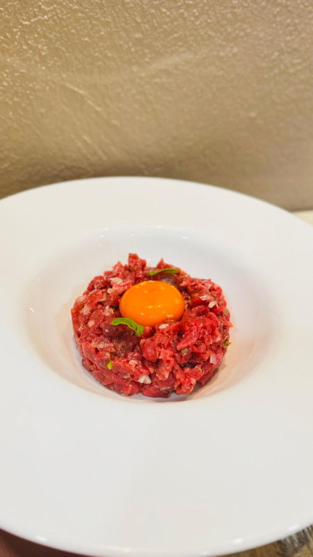 Tartare di manzo con tuorlo d'uovo su un piatto bianco.