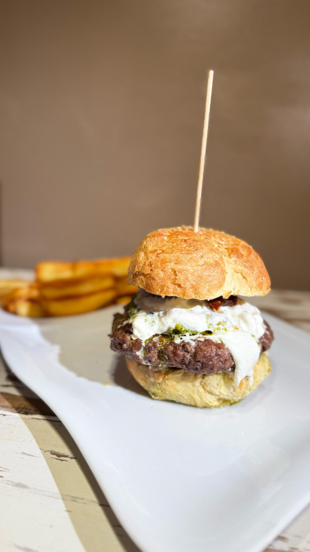 Hamburger servito su un piatto bianco con patatine fritte. L'hamburger è guarnito con besciamella e uno stuzzicadenti.