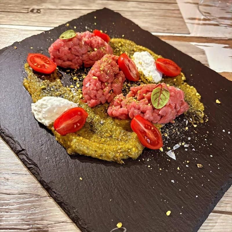 Piatto di carne cruda con pomodori, salsa e formaggio, servito su una lavagna.