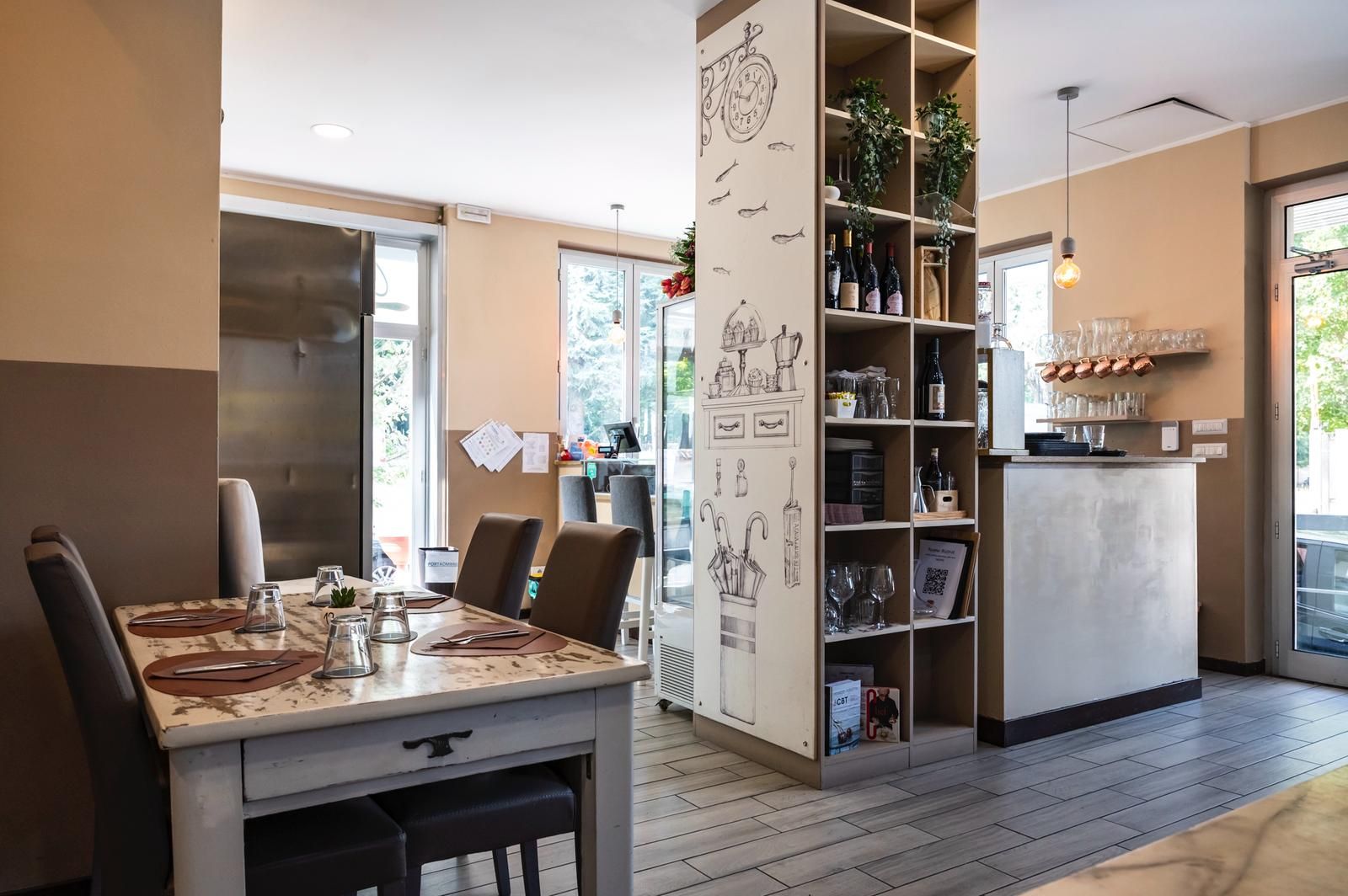 Interno del ristorante: tavolo da pranzo apparecchiato per quattro, scaffale con bottiglie di vino, bancone e porta aperta.