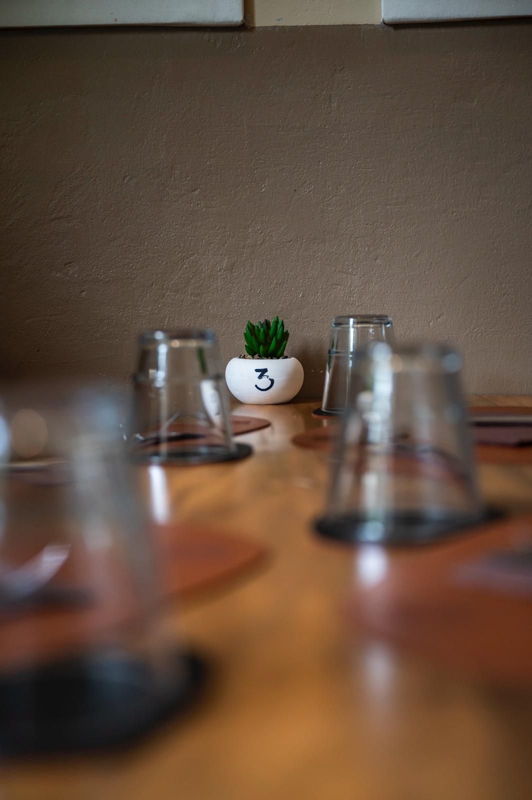 Apparecchiatura della tavola con bicchieri capovolti, una piccola pianta grassa in un vaso bianco con il numero 3.