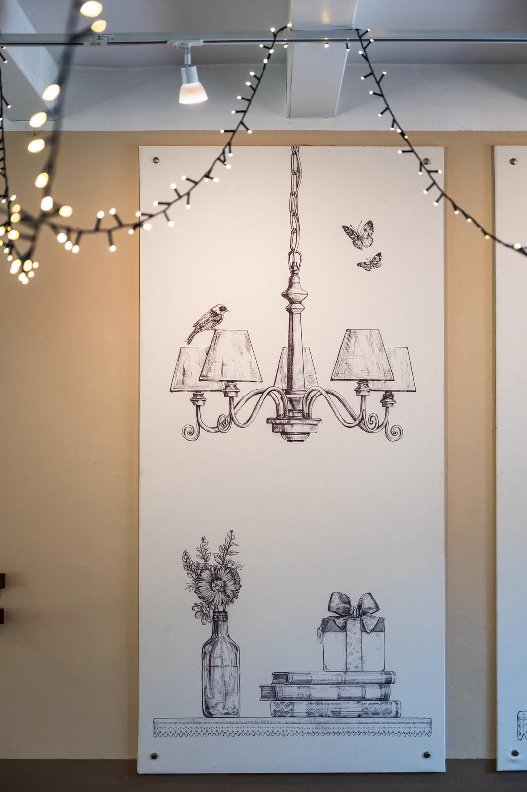 Illustrazione in bianco e nero di un lampadario, fiori e regali su un pannello bianco, decorato con luci a filo.